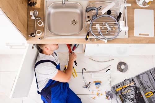 Team member in blue overalls repairing sink